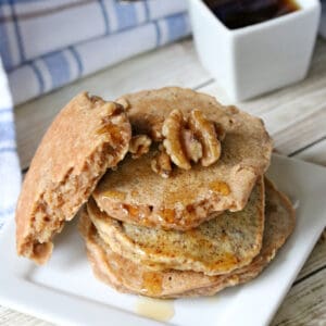 3 low carb walnut pancakes on a white plate with walnuts and maple syrup.