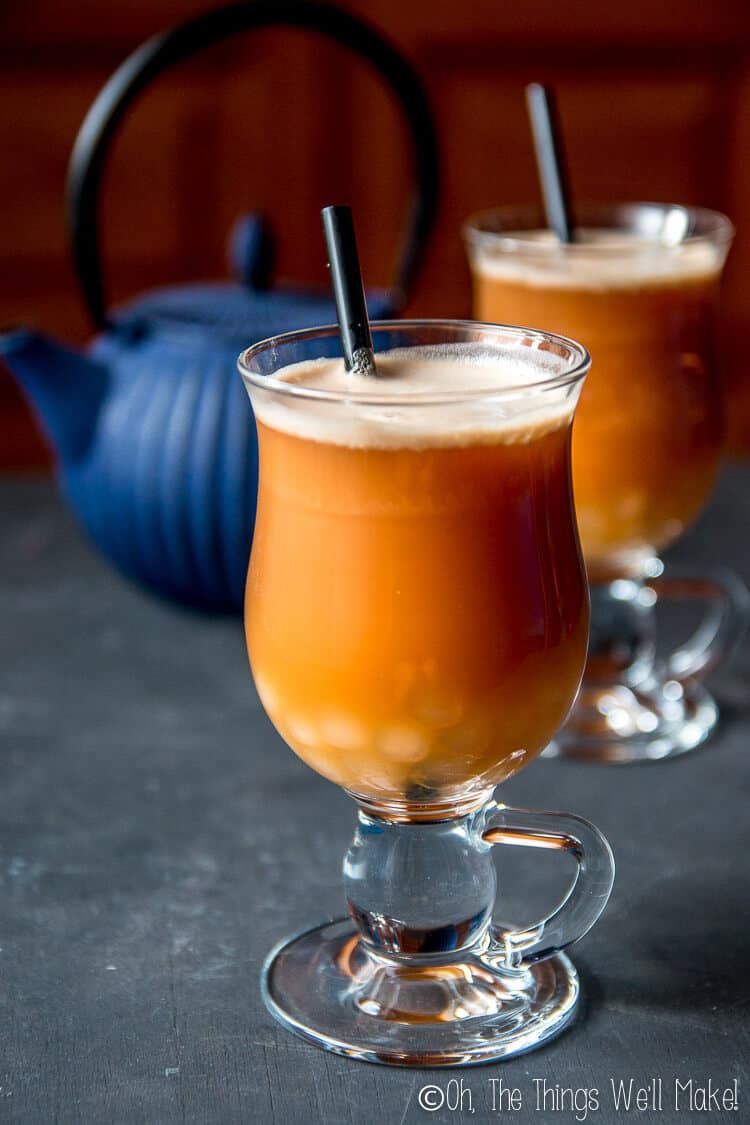 2 glasses of chai latte with homemade boba in front of a blue tea kettle.