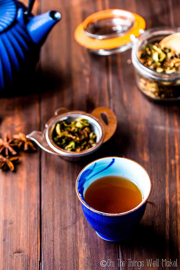 A freshly brewed cup of chai tea with a tea strainer, loose leaf tea, and blue tea kettle