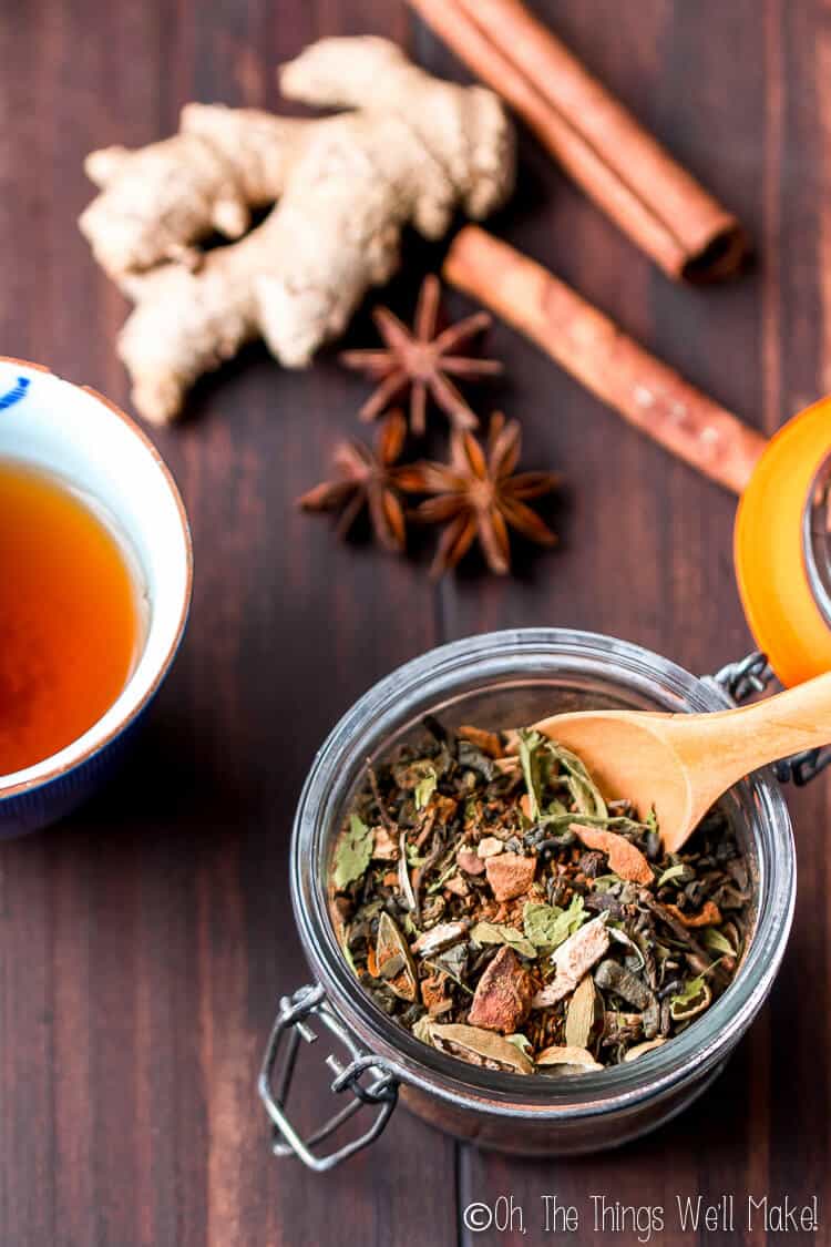 Overhead view of loose leaf chai tea in a small glass jar with spices and a glass of brewed chai