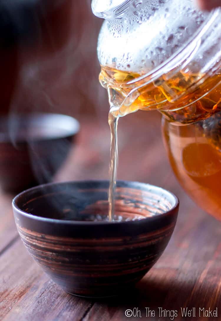 Pouring a steamy glass of hot chai tea from a glass kettle into a brown bowl