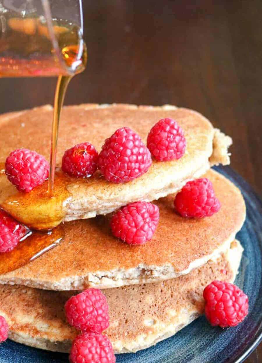 Almond pancakes stacked on a plate and covered with raspberries and maple syrup.