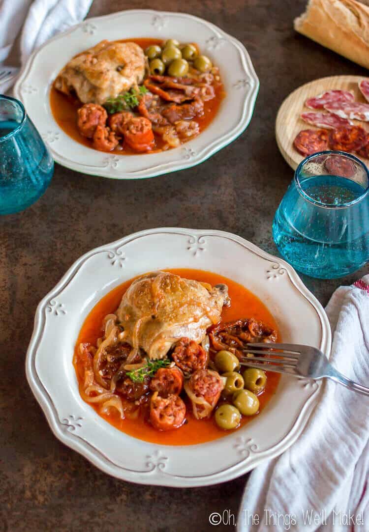 Basque chicken served on plates with chorizo, olives, sun dried tomatoes, and onions.