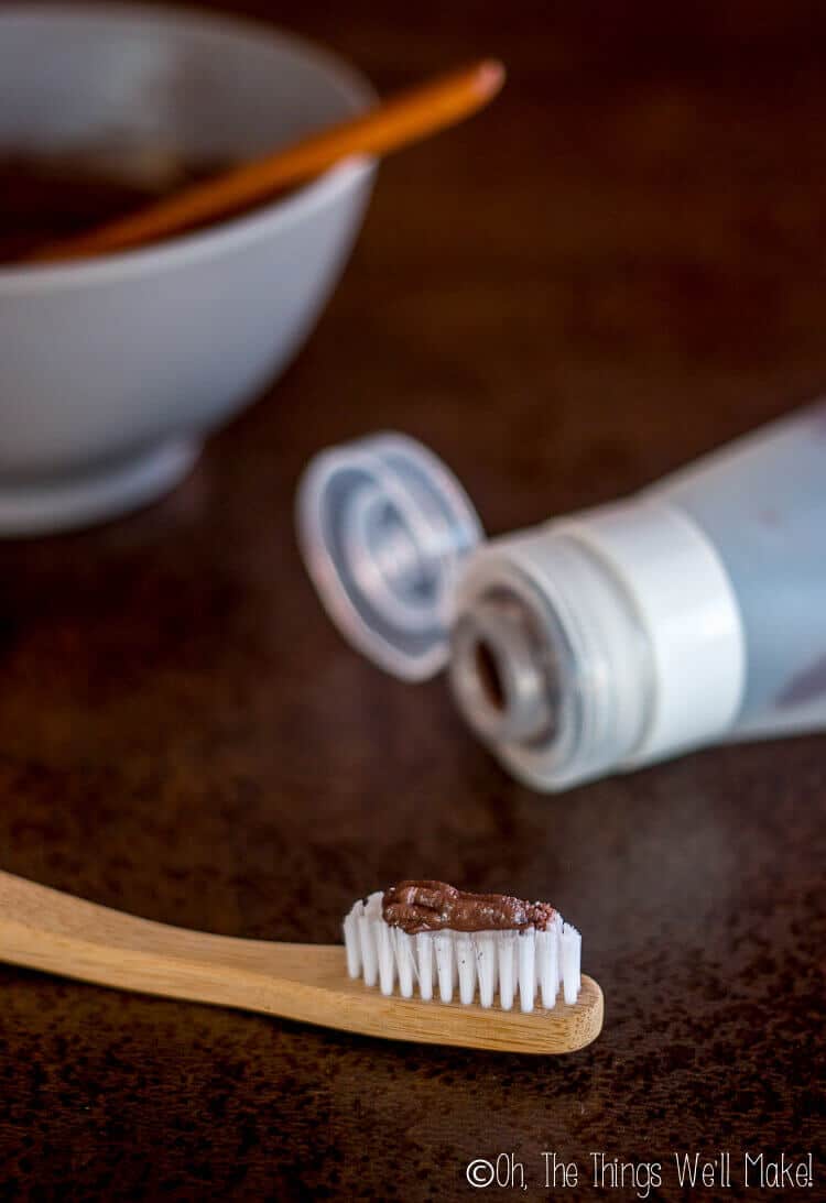 Homemade chocolate toothpaste on bamboo toothbrush below silicone travel tube of toothpaste