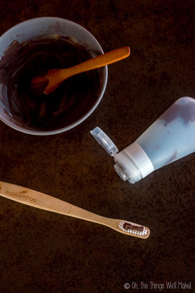 Overhead view of a bowl and silicone tube of homemade toothpaste with some applied to a bamboo toothbrush.