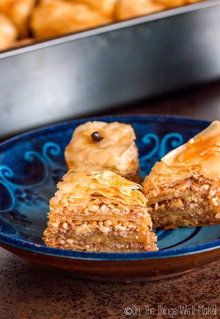 Photo of 3 pieces of baklava on a plate in front of a pan full of baklava.