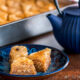 3 pieces of baklava on a plate in front of a tray of baklava