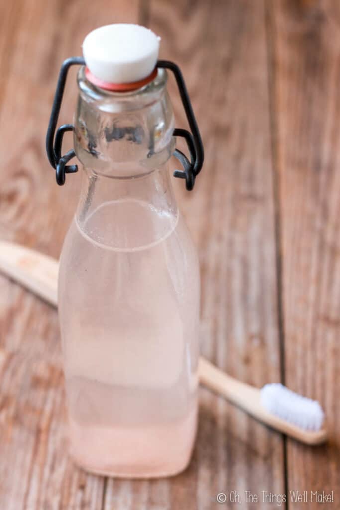 A bottle of homemade natural mouthwash next to a natural bamboo toothbrush.