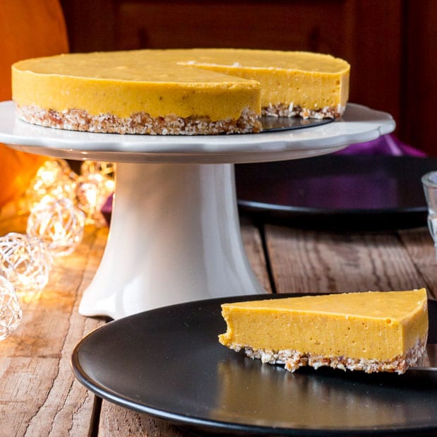 paleo pumpkin pie on a platter, with one slice being served on a plate in front of it.