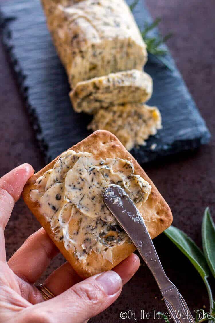 An herbal compound butter being spread onto a cracker