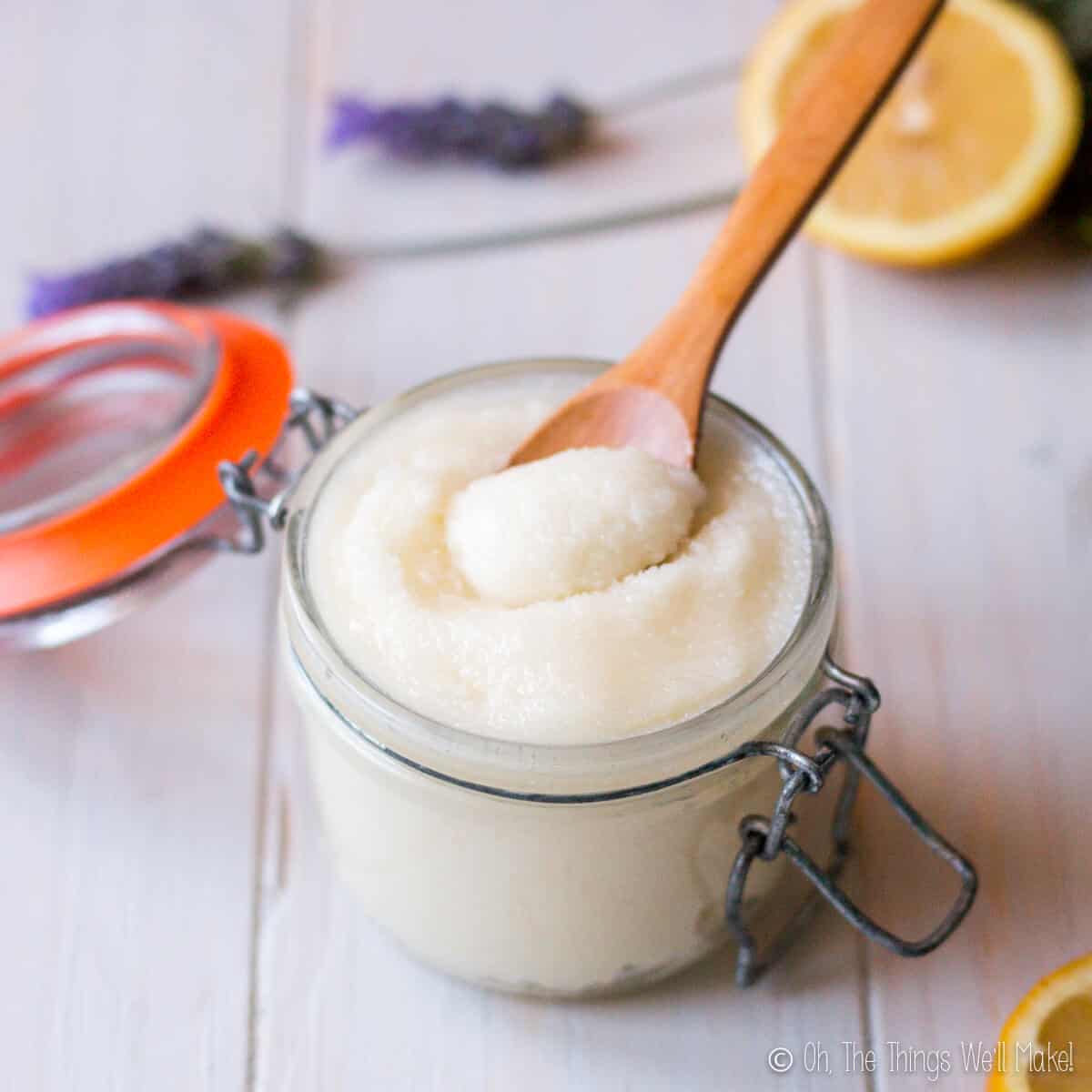 A small glass jar filled with an emulsified sugar scrub with a wooden spoon in it.