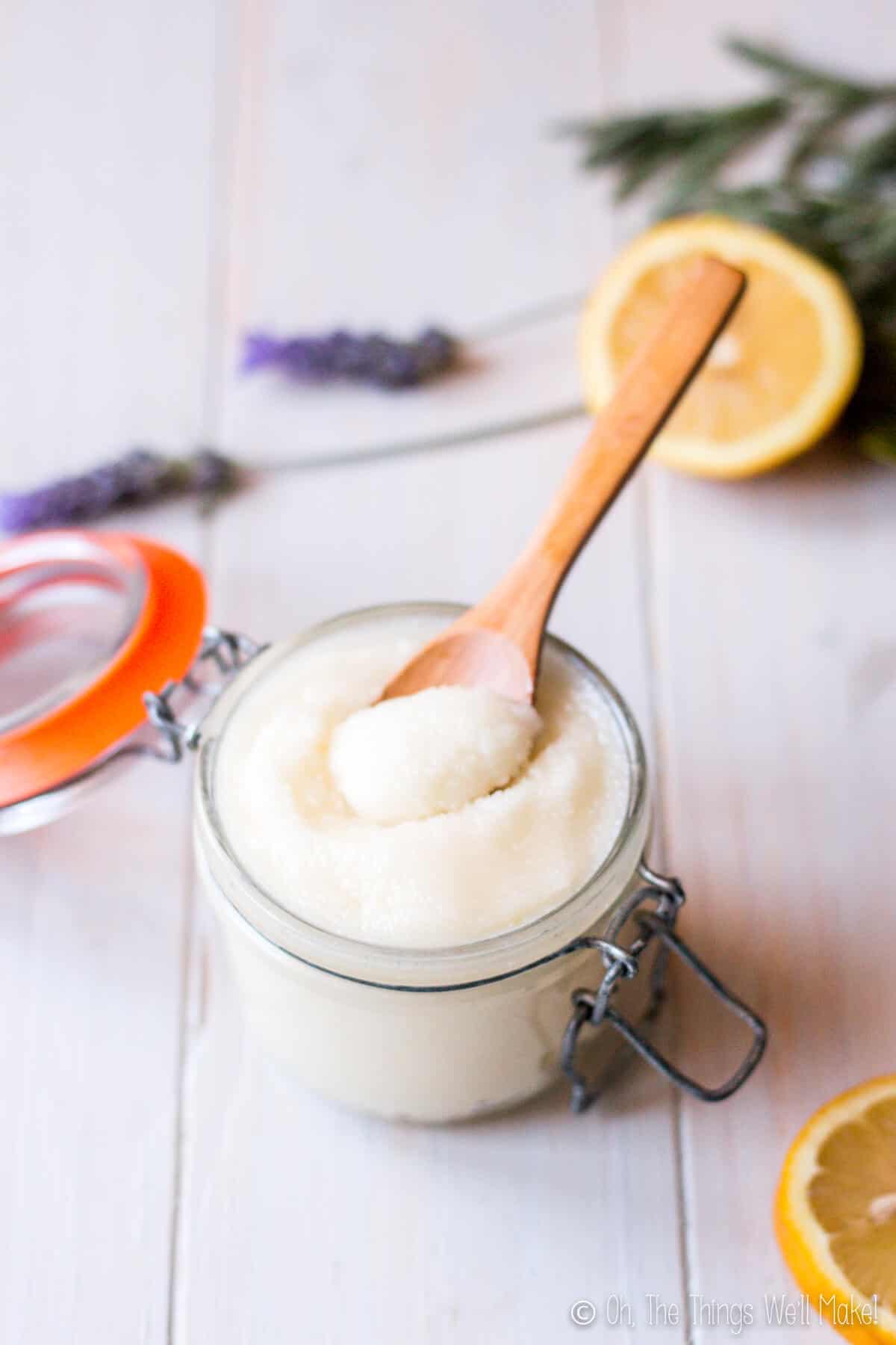 easy emulsified sugar scrub in a glass jar with a wooden spoon with lemon slices and lavender flowers