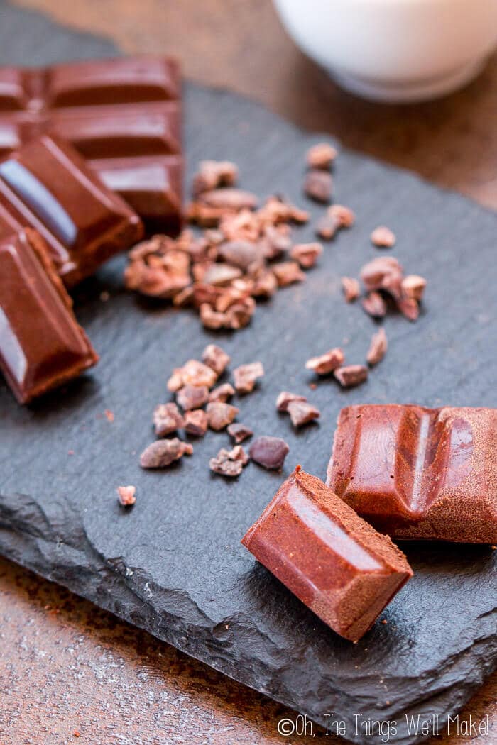 Homemade milk chocolate pieces in front of cocoa nibs and homemade dark chocolate