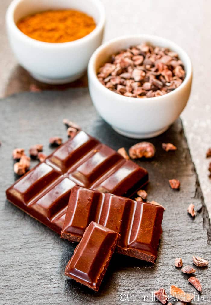 Homemade chocolate bars on a slate tile with cocoa nibs and coconut sugar in the background