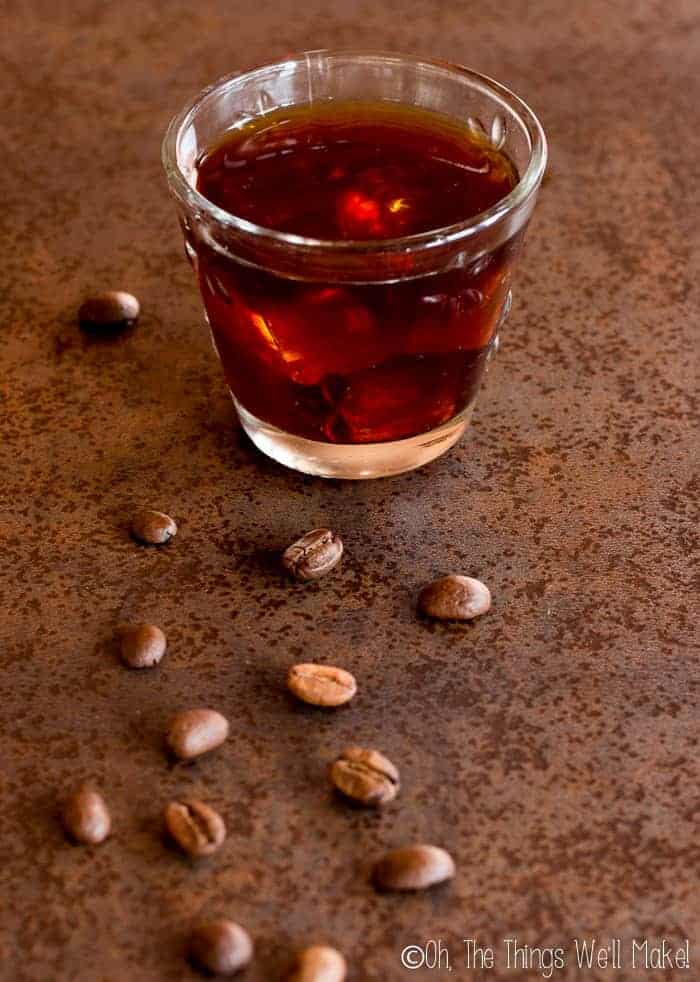 a glass of cold brew coffee with ice surrounded by coffee beans