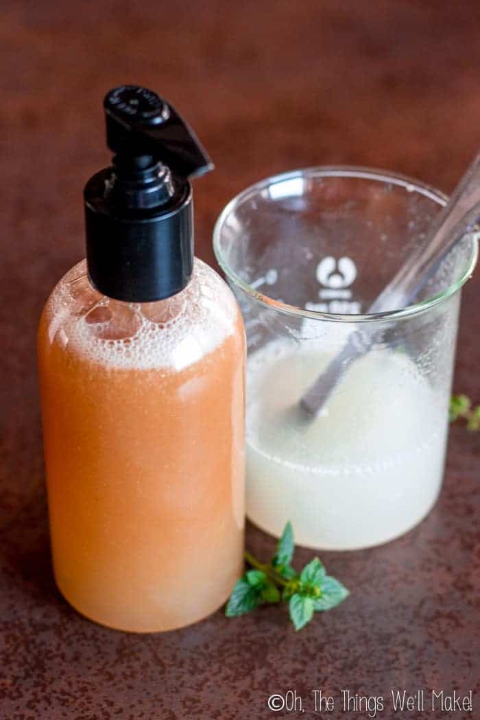 A photo of a brown shampoo made with a peppermint tea next to a beaker with the same shampoo made with distilled water instead, the latter being a white color.