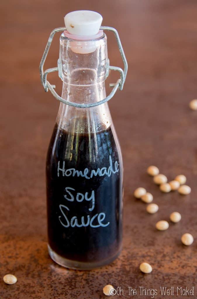 A bottle of homemade soy sauce with the words "homemade soy sauce" written on the bottle and soy beans around it.