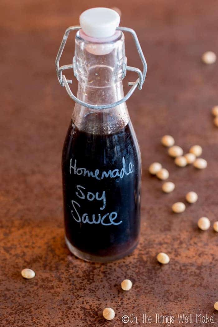 A bottle of homemade soy sauce on a counter surrounded by dried soybeans.