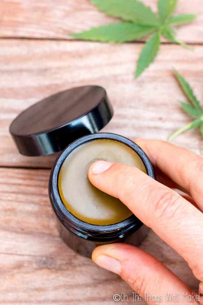 Pressing a finger into a homemade CBD salve for application of the salve