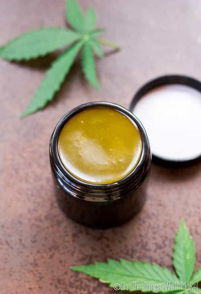 An open jar of homemade CBD salve with cannabis leaves on a brown countertop