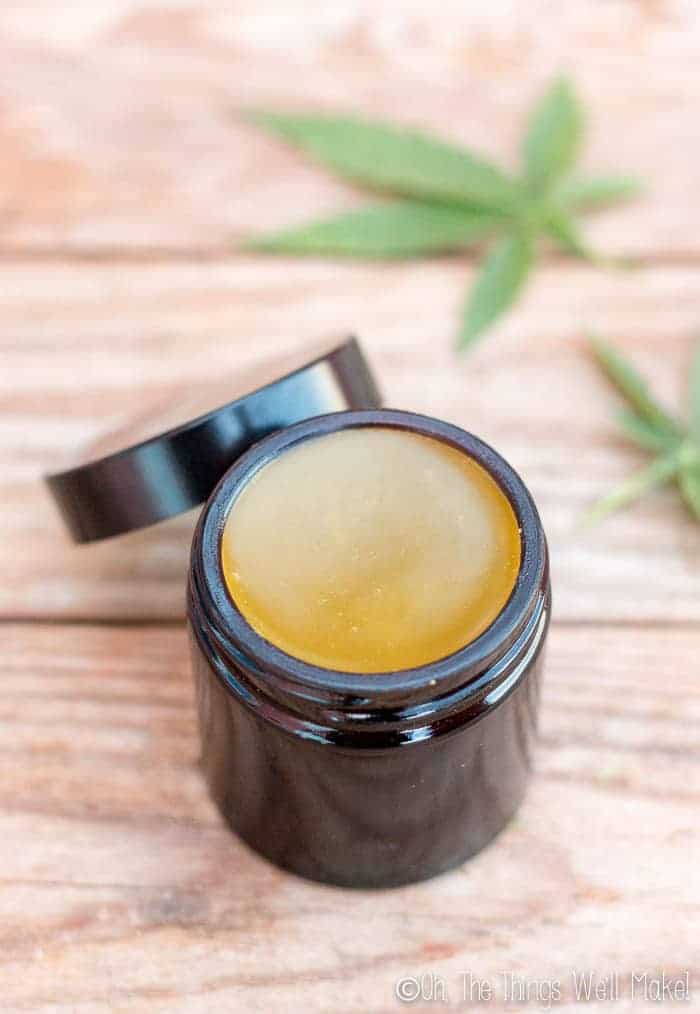 An open jar of homemade CBD salve in a glass amber jar on a wooden background