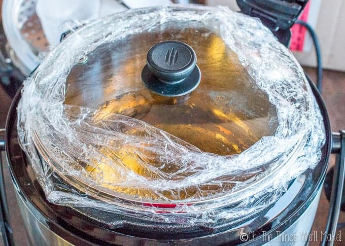 Crock pot filled with glycerin soap and solvents, covered and sealed with plastic wrap.