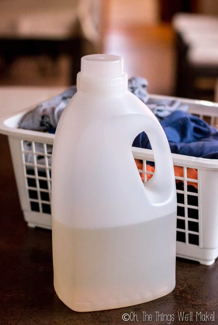 a bottle of ahomemade laundry detergent in front of a basket of folded clothes.