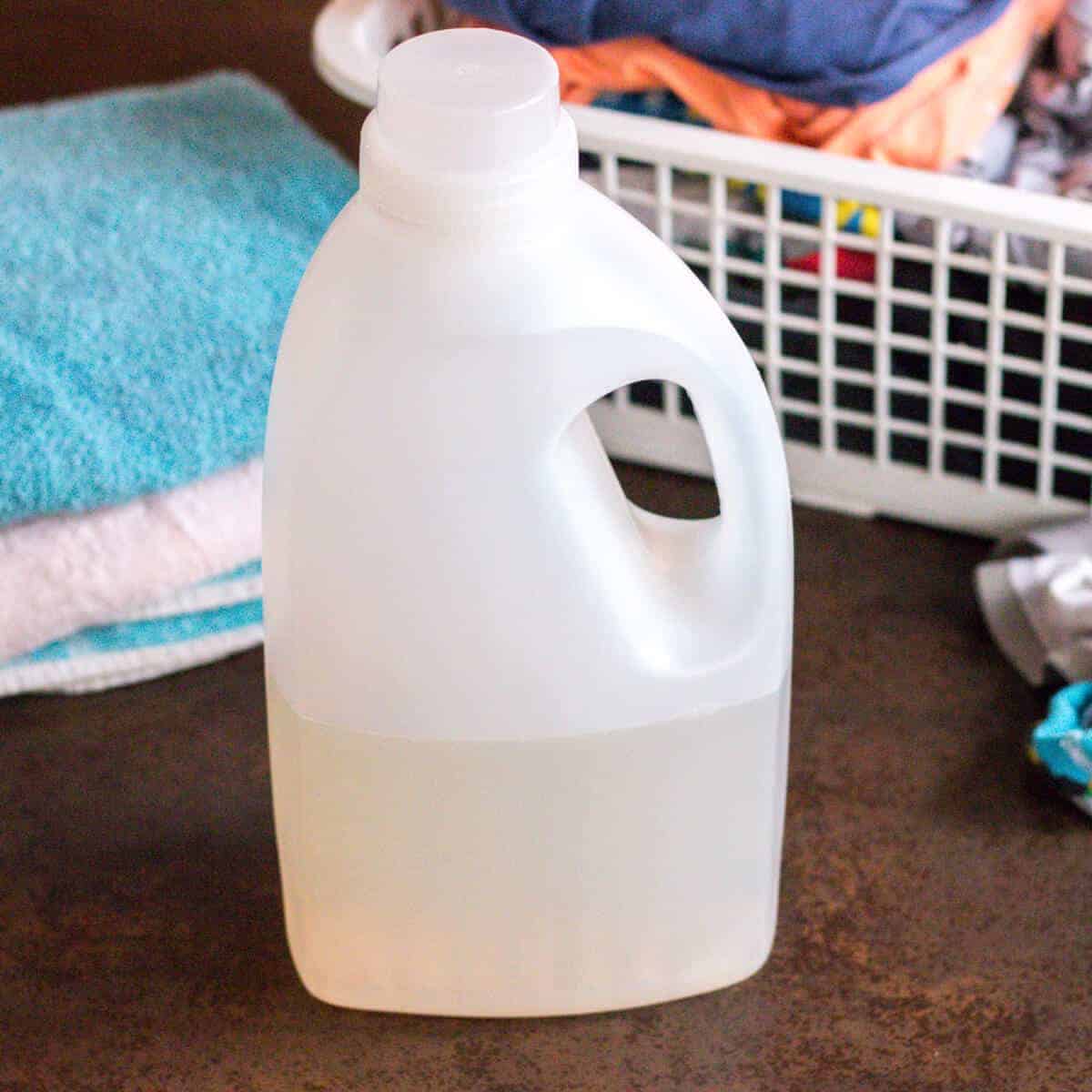 A plastic bottle filled with a homemade laundry detergent in front of a load of folded laundry
