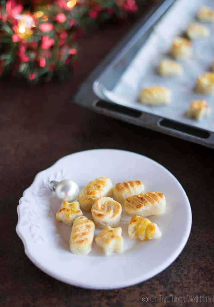 Close-up of homemade marzipan figures on a plate in front of a baking sheet full of more marzipan figures.