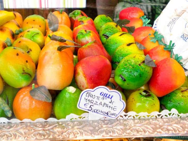 Two layers of multi-colored marzipan fruit figures in a store window in Italy.