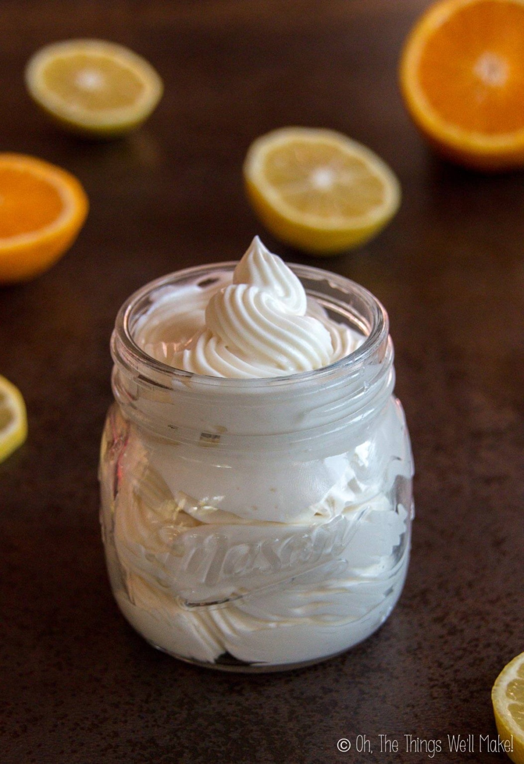 A jar of DIY whipped body butter surrounded by slices of citrus fruits.