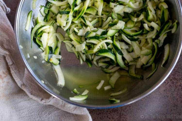 A bowl of julienned zucchini with salt showing the liquid being release from the zucchini.