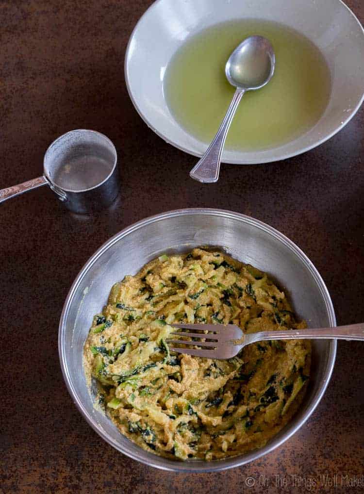 Two bowls, one with the liquid released from the zucchini, and another filled with the zucchini and batter mixture.