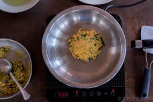 A zucchini pancake (hobakjeon) being fried in a stainless steel frying pan.