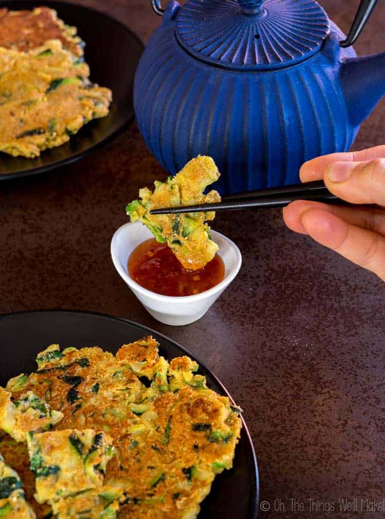 dipping a piece of zucchini pancakes (hobakjeon) into sweet and sour sauce with chopsticks.