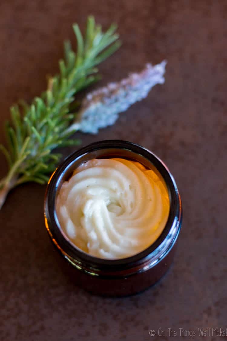 A jar of hair butter as seen from overhead with a sprig of rosemary and a lavender flower