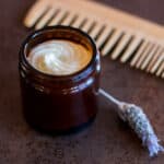 A jar filled with a homemade hair butter next to a sprig of lavender and a wooden comb