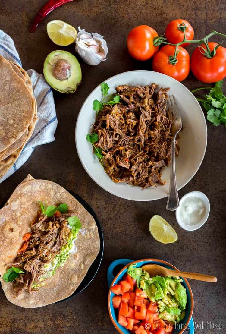 Overhead view of shredded beef for chipotel beef tacos, served with guacamole, tomatoes, and homemade flour tortillas.