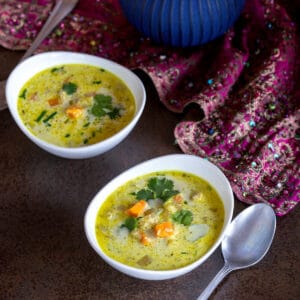 Overhead view of two bowls of chicken mulligatawny soup next to a blue teapot