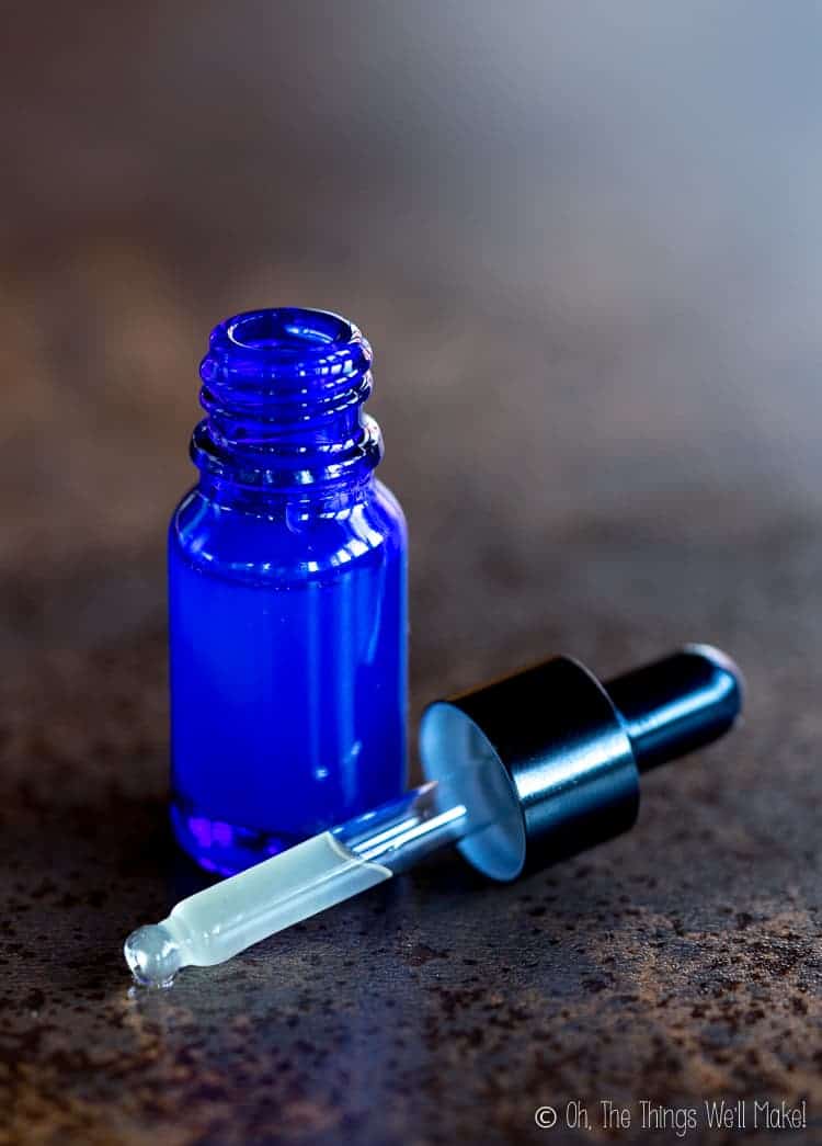 A small glass blue bottle filled with a hyaluronic acid serum. The glass pipette is out and in front of the bottle, showing some of the serum inside it.