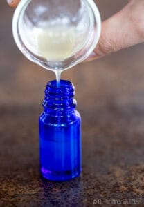 Pouring a homemade hyaluronic acid serum into a blue glass bottle.