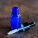 A small glass blue bottle filled with a hyaluronic acid serum. The glass pipette is out and in front of the bottle, showing some of the serum inside it.