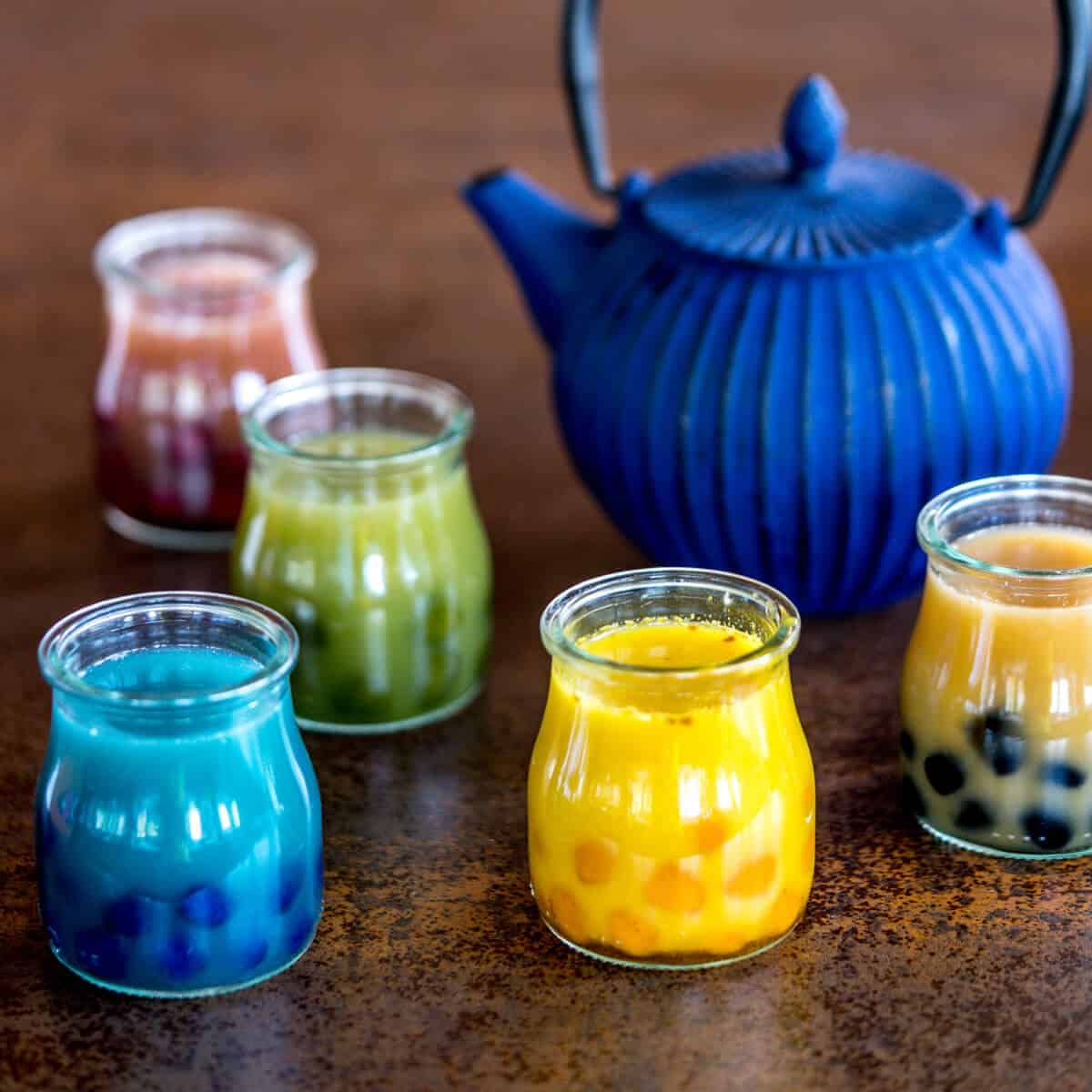 5 glasses filled with different colored drinks with multiple colors of boba.
