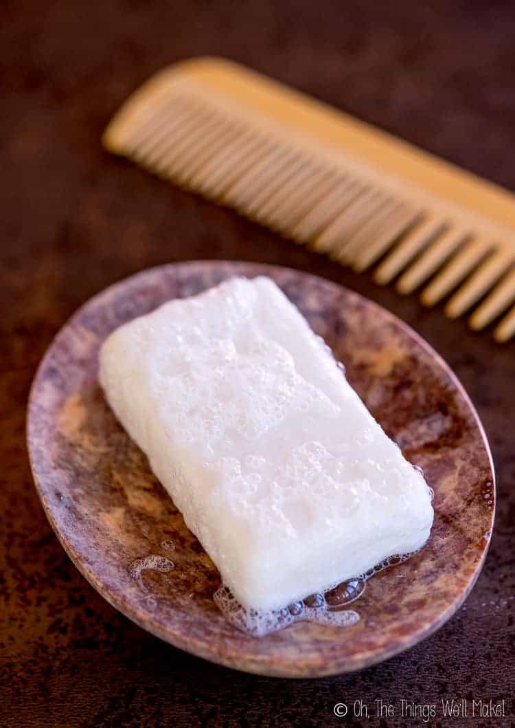 Overhead view of a homemade shampoo bar in a stone soap dish, next to a bamboo comb