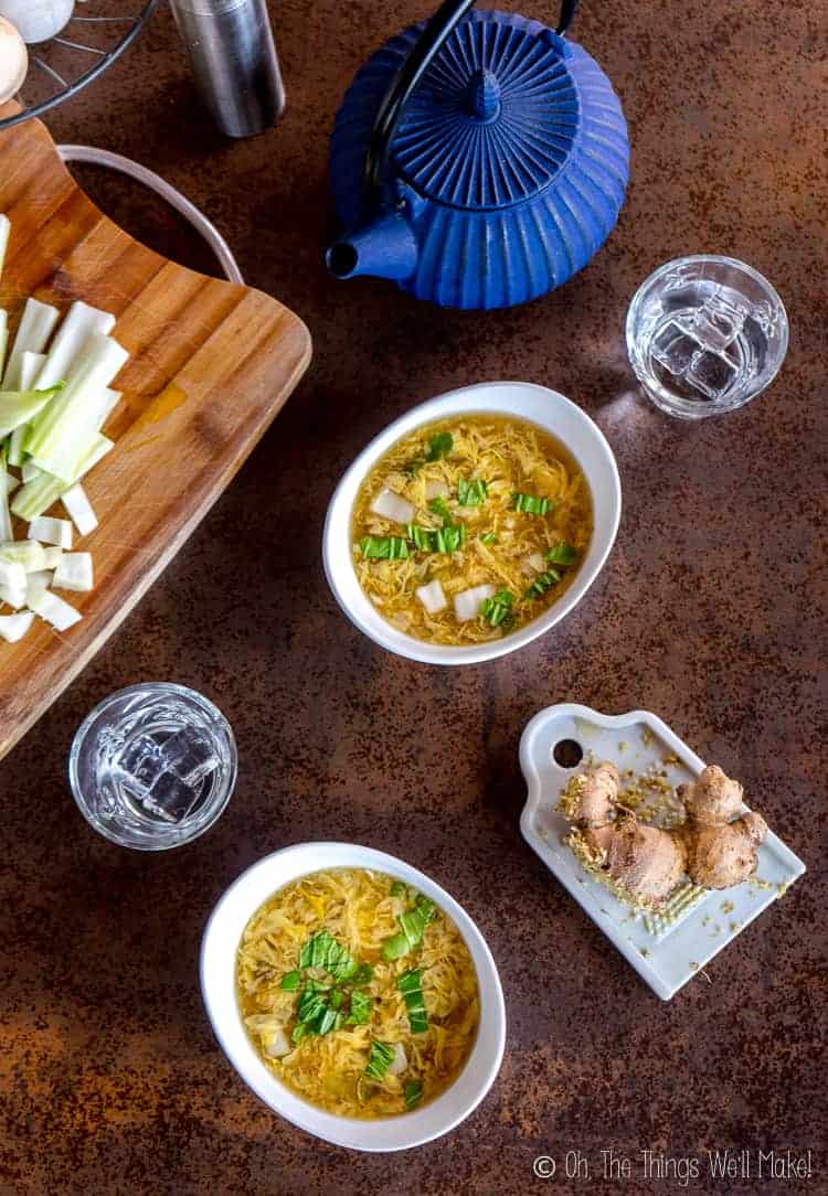 Overhead view of 2 bowls of homemade egg drop soup with ginger, bok choi, and a teapot