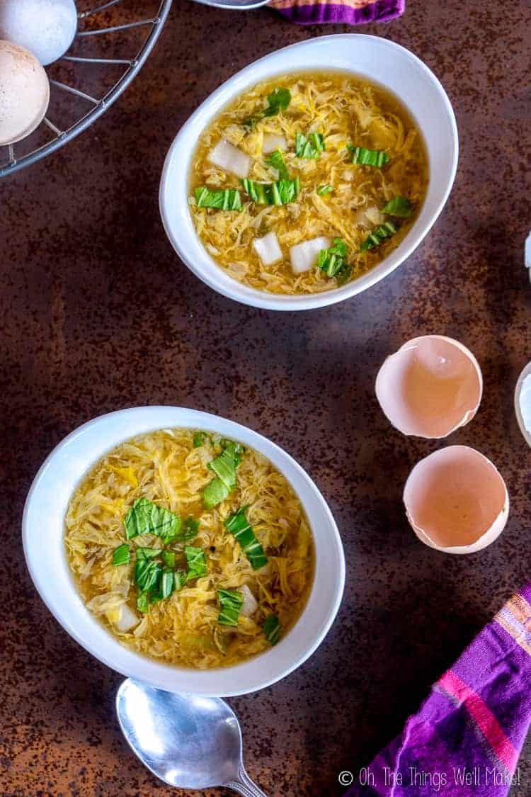 Overhead closeup view of two bowls of paleo egg drop soup with eggs and eggshells.