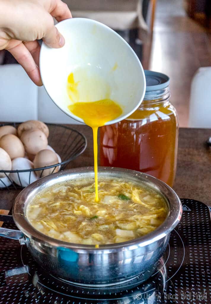 A photo of egg mixture being poured into the soup in a thin stream.