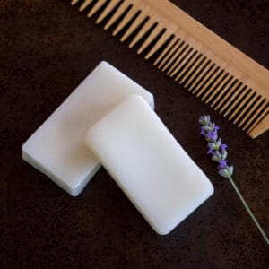 Two homemade conditioner bars on a counter with a sprig of lavender and a wooden comb