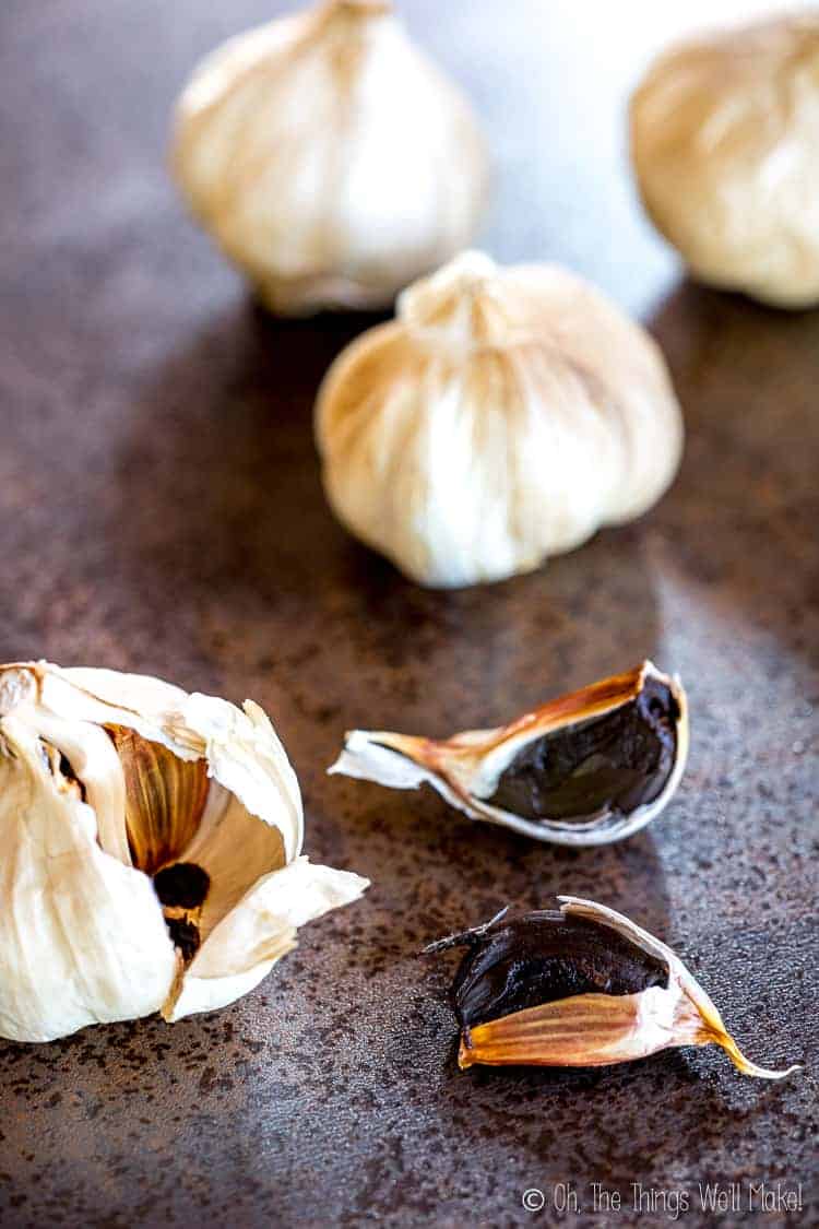 Several heads of black garlic with one open showing the black cloves. 