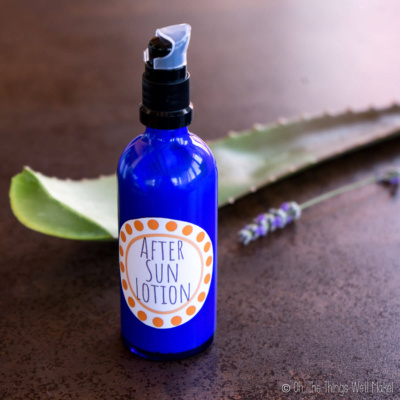 A bottle of homemade after sun lotion in front of an aloe leaf and a lavender flower